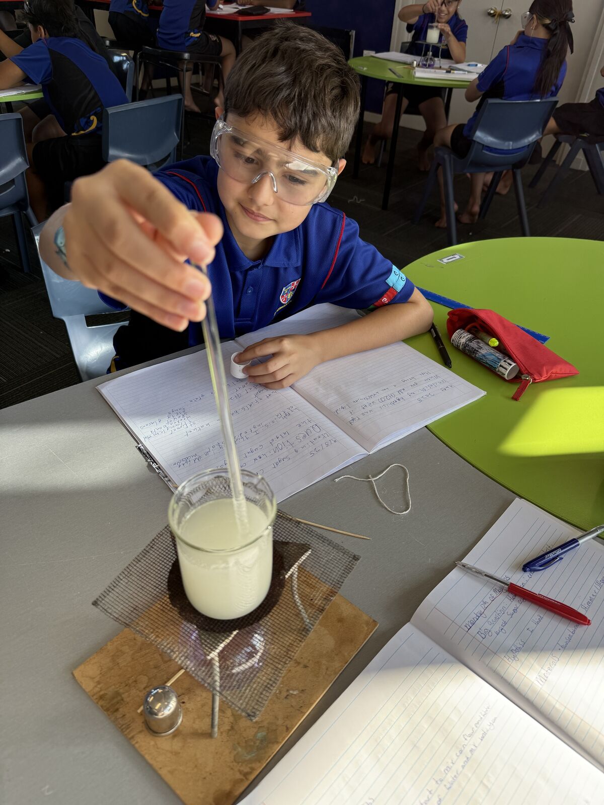 Student wearing safety goggles conducting a science experiment by heating a liquid in class.