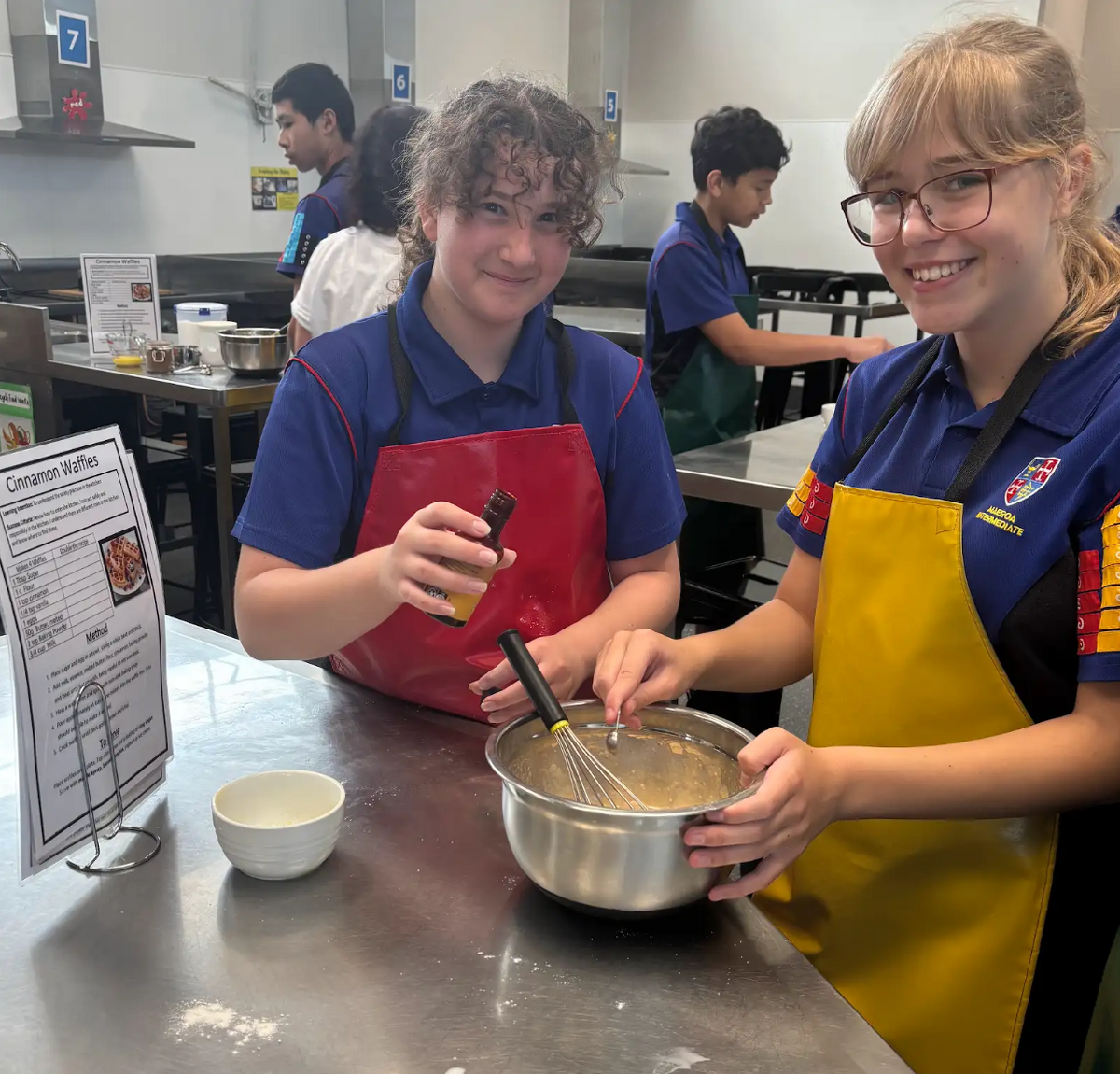 Group of students wearing aprons and standing by prepared food in a cooking class.